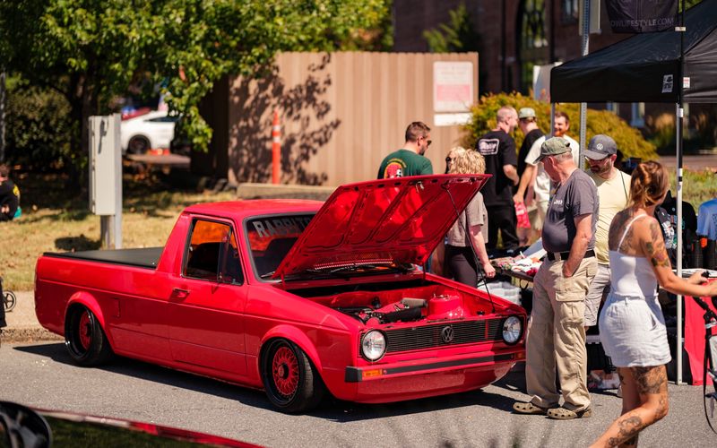 A black Volkswagen GTI Mk2 with its hood open on a city street, drawing a crowd of onlookers